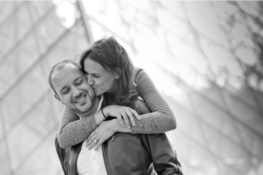 Couple qui s'enlace devant la pyramide du Louvre lors d'une session photo à Paris.